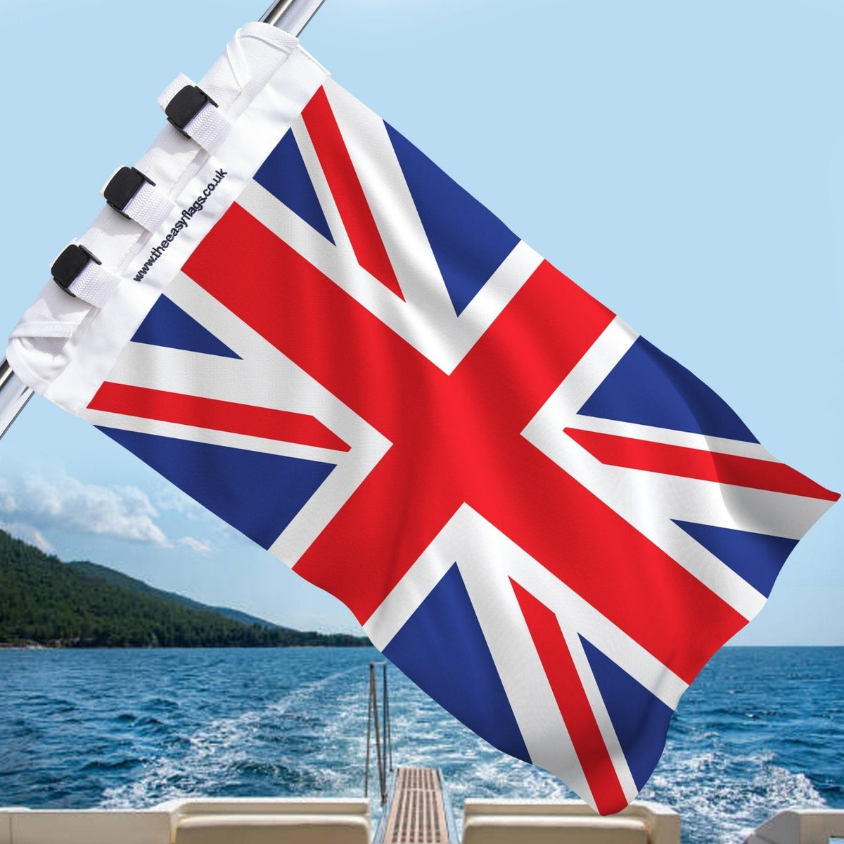 Union Jack flag with red, white, and blue design, mounted on a boat rail with a universal triple-lock system, flying at sea with blue sky and coastline in the background