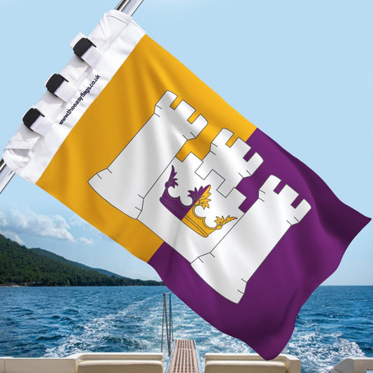Aberdeenshire county flag with gold and purple background, featuring a white triple-towered castle and crown emblem, mounted on a boat rail with a universal triple-lock system, flying at sea with blue sky and coastline in the background