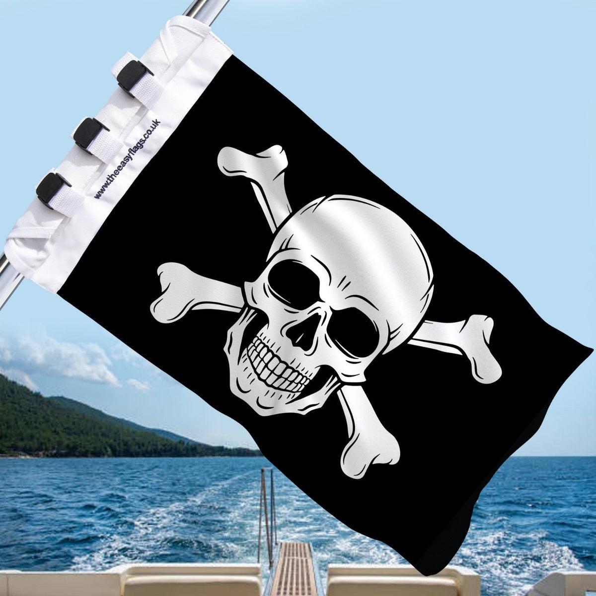 Black Jolly Roger pirate flag with skull and crossbones, mounted on a boat rail with a universal triple-lock system, flying at sea with blue sky and coastline in the background