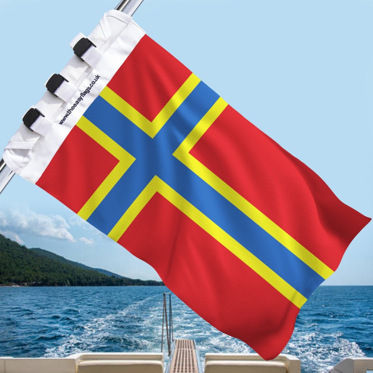 Orkney county flag with red background and blue Nordic cross outlined in yellow, mounted on a boat rail with a universal triple-lock system, flying at sea with blue sky and coastline in the background