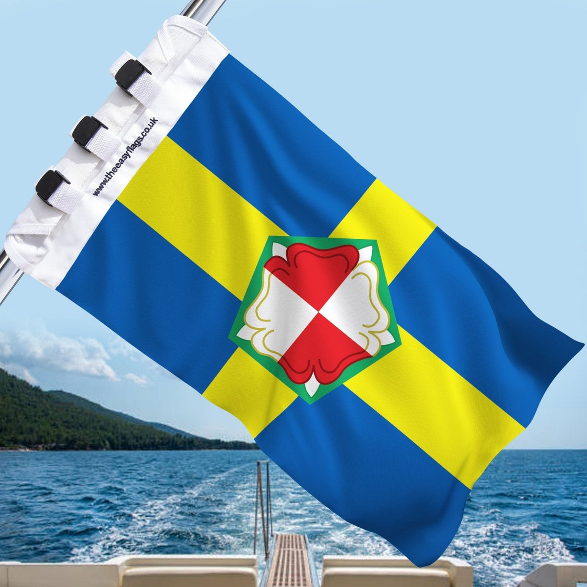 Pembrokeshire county flag with blue background, yellow cross outlined in red and Tudor rose, mounted on a boat rail with a universal triple-lock system, flying at sea with blue sky and coastline in the background
